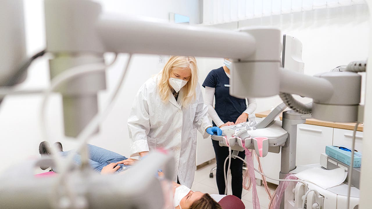 Female doctor with a protective face mask doing a breast scan to the patient