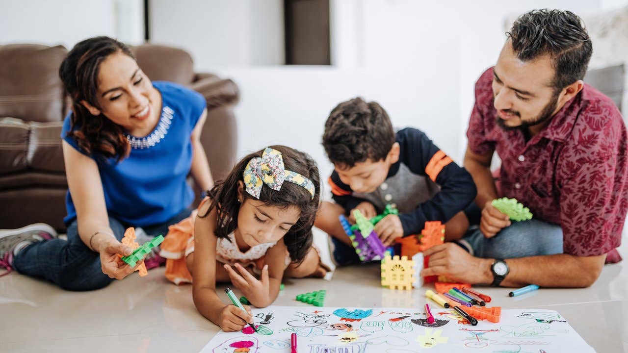 Smiling Hispanic/Latino family - mom, dad, daughter and son - at home drawing pictures and playing games together