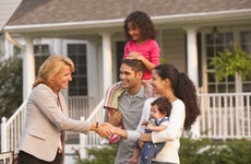 A young family meets with a realtor outside a home with a for sale sign outside