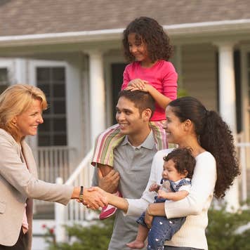 A young family meets with a realtor outside a home with a for sale sign outside