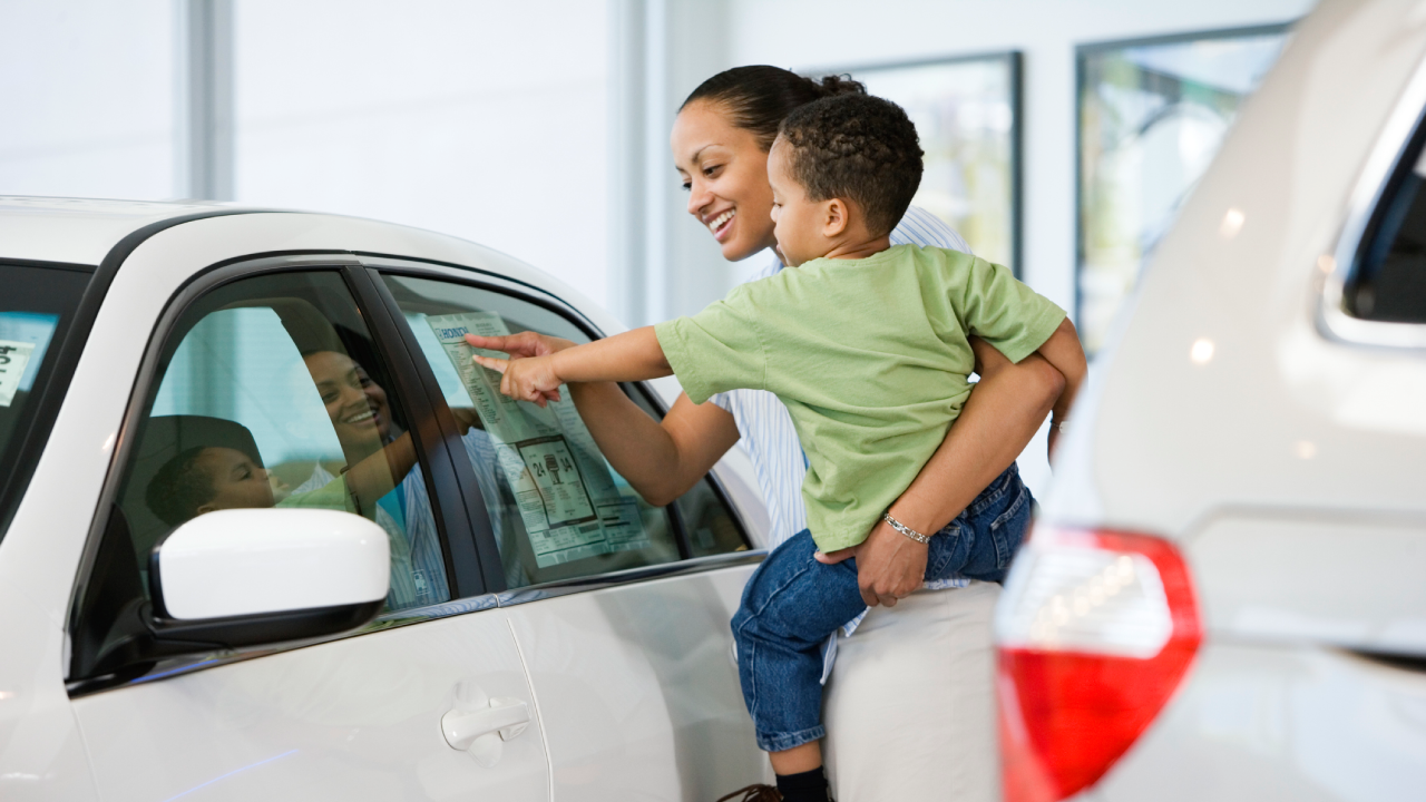 Parent and child looking at a white car on the showroom floor of a dealership.