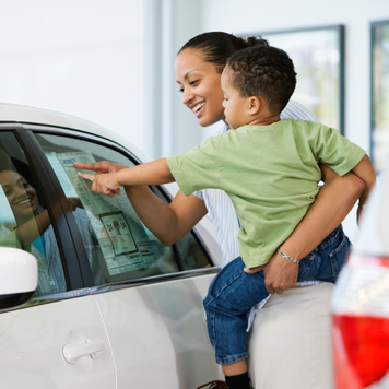 Parent and child looking at a white car on the showroom floor of a dealership.