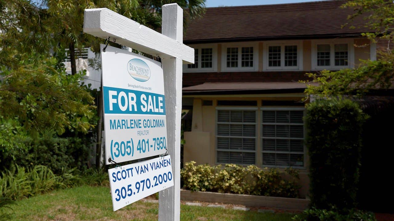 Suburban Florida home with trees, green lawn, white "for sale" sign outside