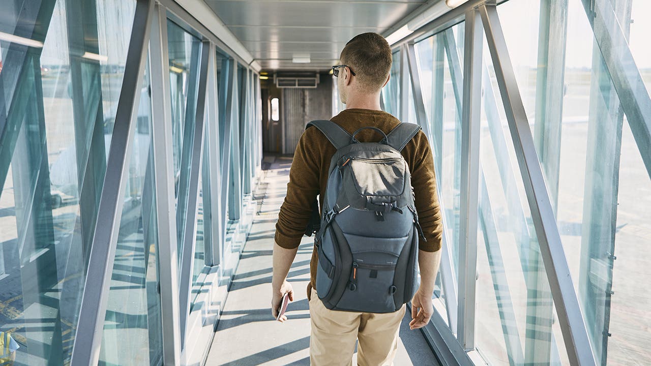 Rear view of young man with backpack and passport in hand during boarding at airport.