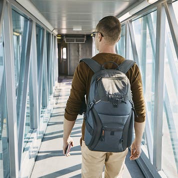 Rear view of young man with backpack and passport in hand during boarding at airport.