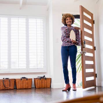 Smiling real estate agent carrying documents while entering home from front door