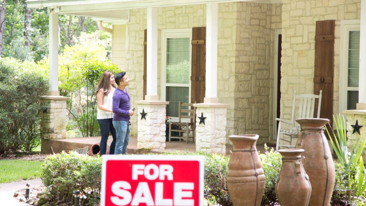 Young couple looking at a home for sale, standing outside a stone front porch