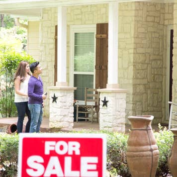 Young couple looking at a home for sale, standing outside a stone front porch