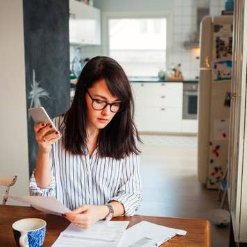 Woman with laptop and smartphone in dining room looking over bills