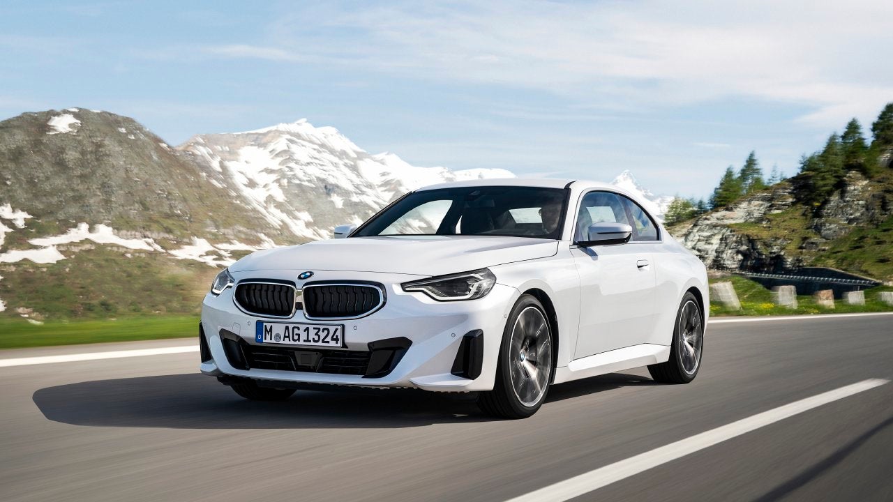 A white 2022 BMW 2 Series driving down the highway against a mountainous backdrop