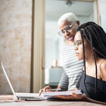 Woman looks over young student's shoulder at laptop