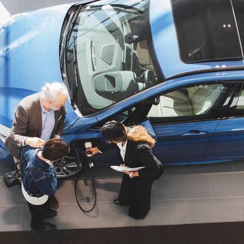 Saleswoman explaining customers to charge electric car at showroom