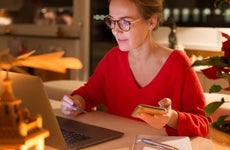 Woman wearing glasses on laptop while holding phone
