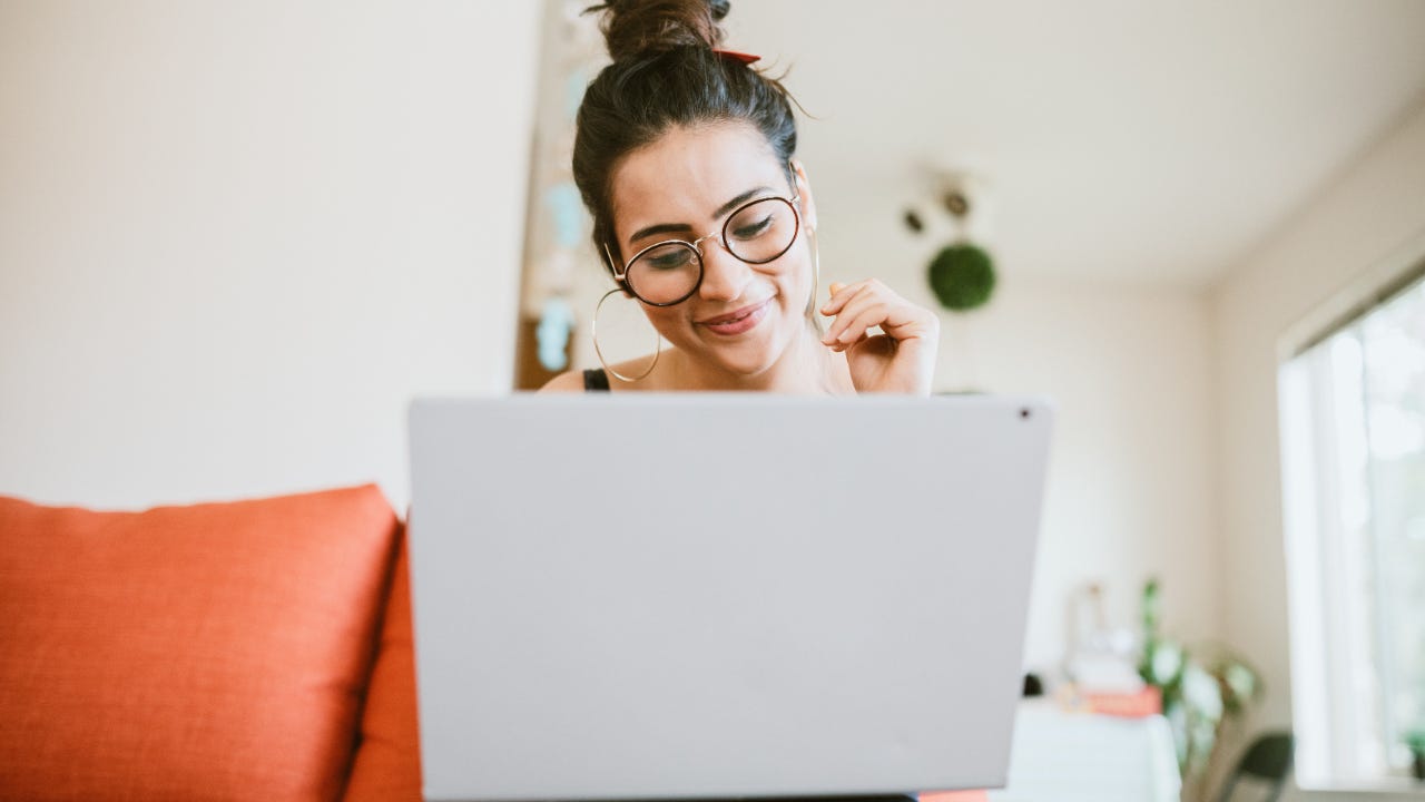 Person with glasses sitting on orange couch smiling at laptop