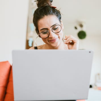 Person with glasses sitting on orange couch smiling at laptop