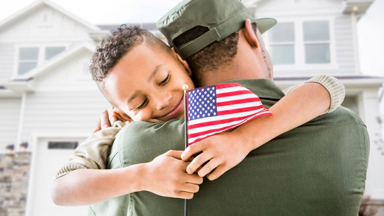 Soldier hugging patriotic son outside house