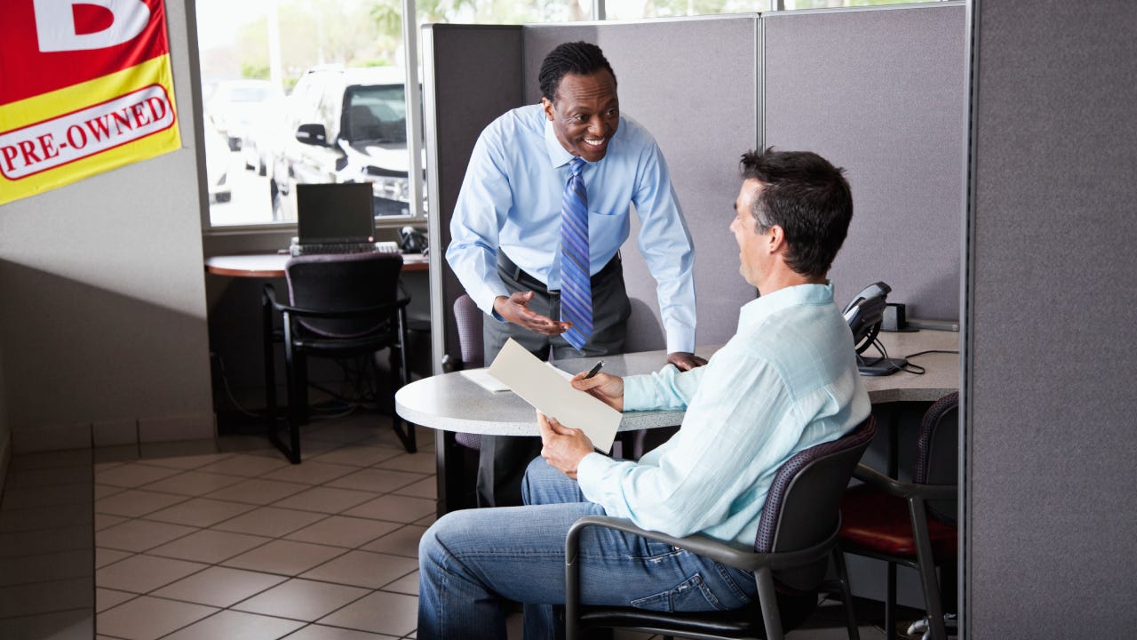 Car salesman with customer signing paperwork to buy used car.