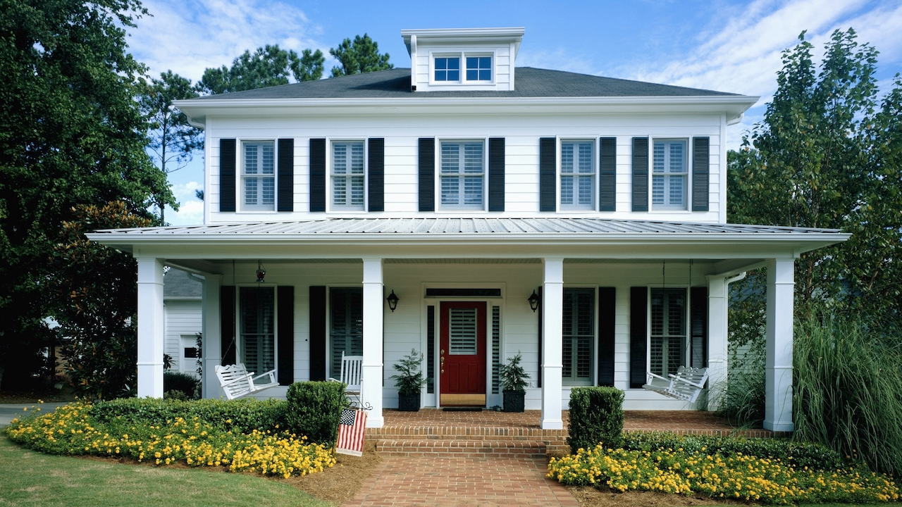 white house with flower beds, a brick driveway and a porch with rocking chairs