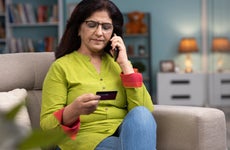 woman on the phone holding a credit card sitting on a couch