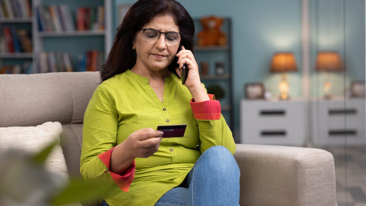 woman on the phone holding a credit card sitting on a couch