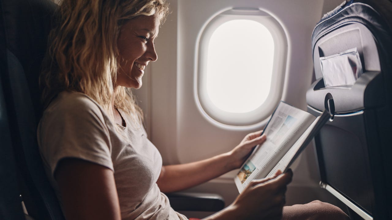 Happy woman reading a magazine in an airplane.