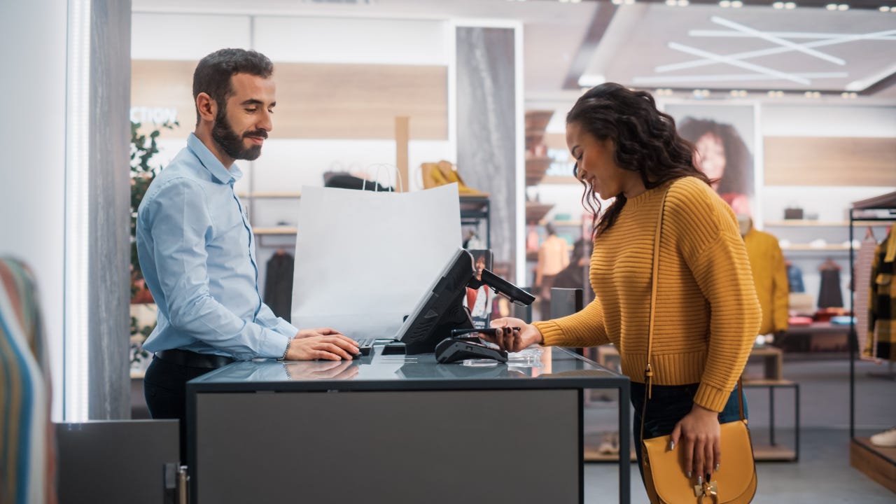 Young Woman at Counter Buys Clothes from Friendly Retail Sales Assistant