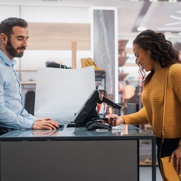 Young Woman at Counter Buys Clothes from Friendly Retail Sales Assistant