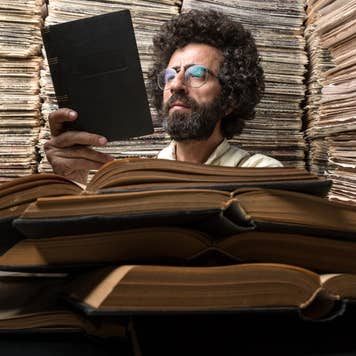Adult man with dark hair reading book for research in archive of printed media