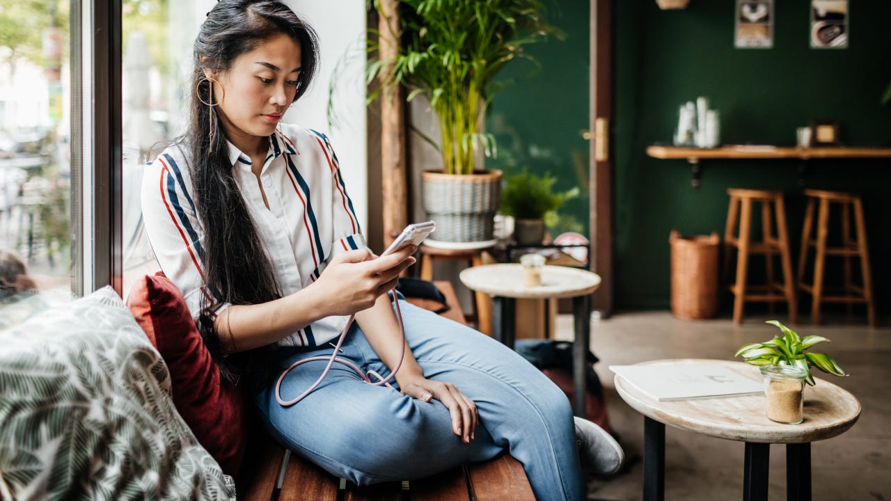 A cafe customer sitting by the window in her favorite cafe, using her smartphone and relaxing.