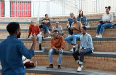 Young male professor teaching multi-ethnic students sitting on amphitheater steps at university campus