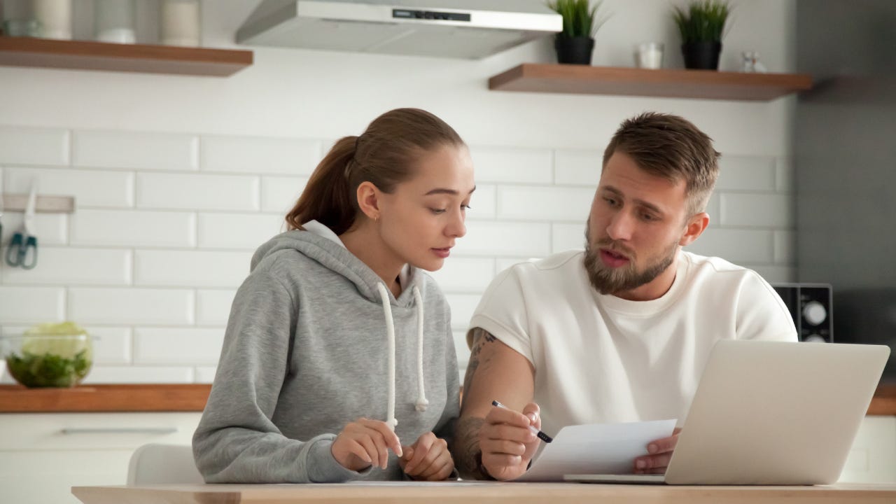 Focused serious couple checking bills sitting together at kitchen table