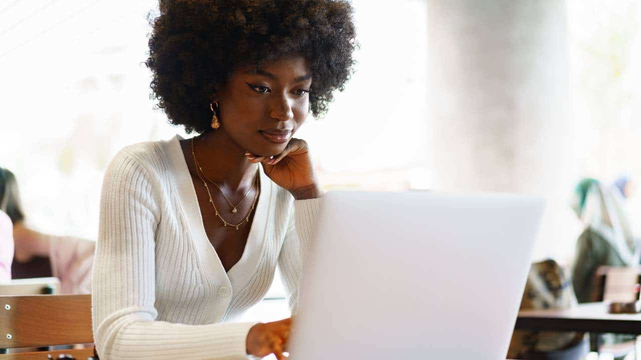 Smiling young african woman sitting with laptop in cafe, portrait