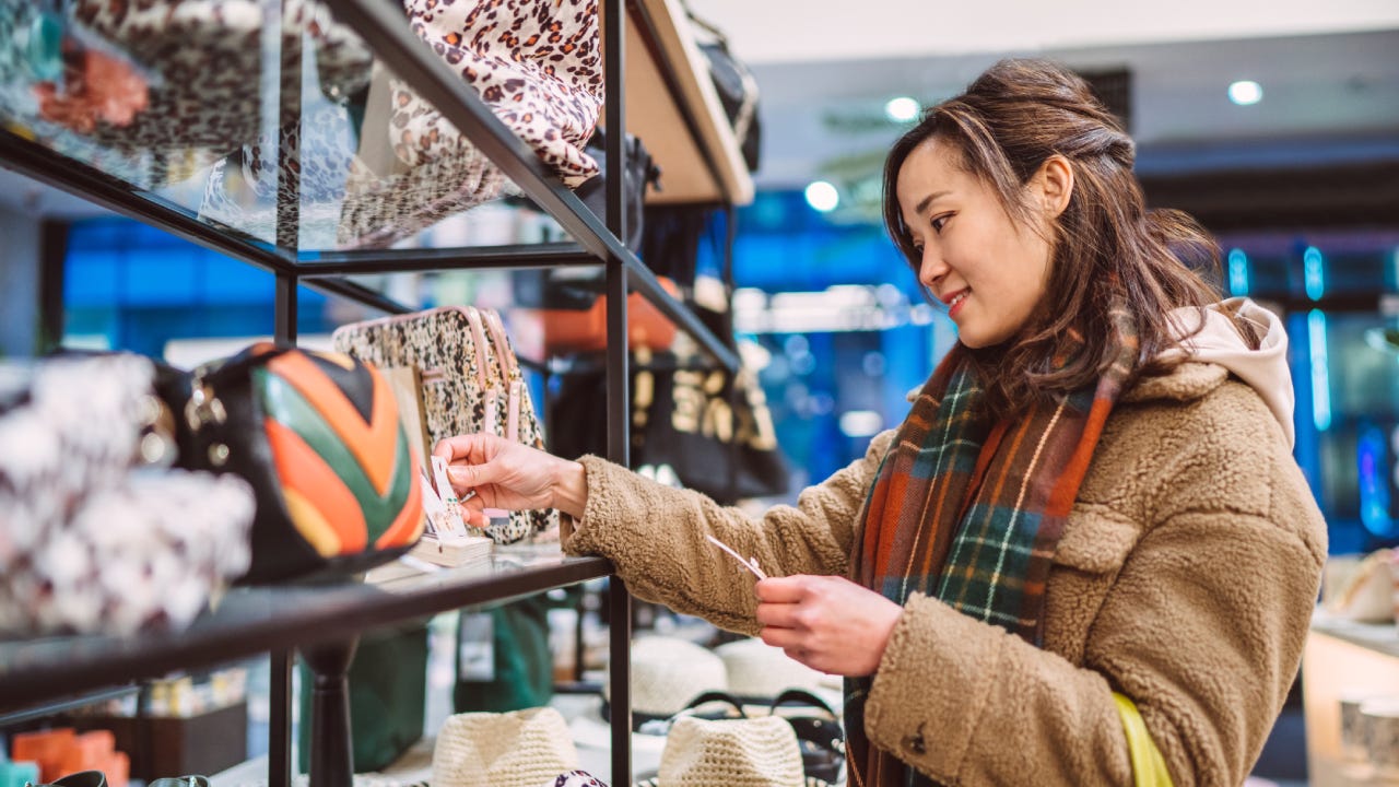 Young cheerful Asian woman shopping for accessories in boutique