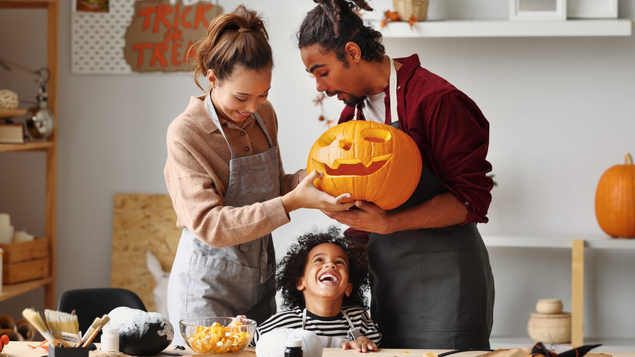Happy african american family mother father and little boy son smiling while making jack o lantern