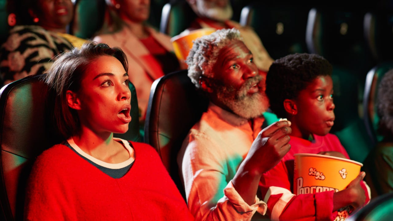 Surprised young woman watching horror movie by spectators in theater