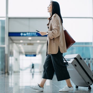 Young woman carrying suitcase and holding smartphone in hand, walking in airport terminal.