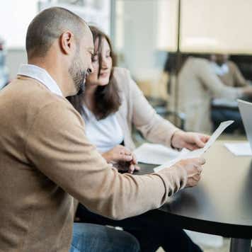 A white man and woman sit together and review paperwork at a dealership.