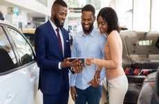 Dealership Center Manager Showing Vehicle Characteristics On Digital Tablet To Young Black Couple