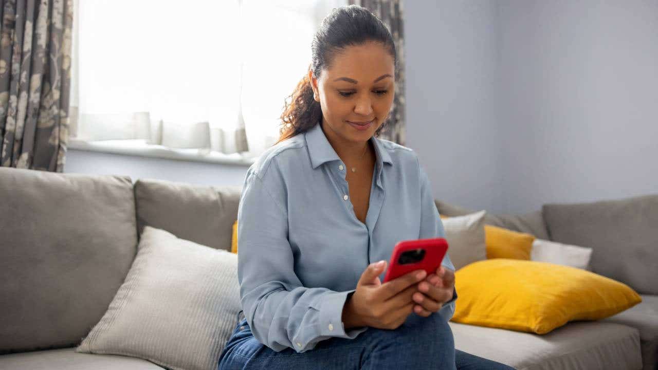 Happy woman at home reading a text message on her cell phone