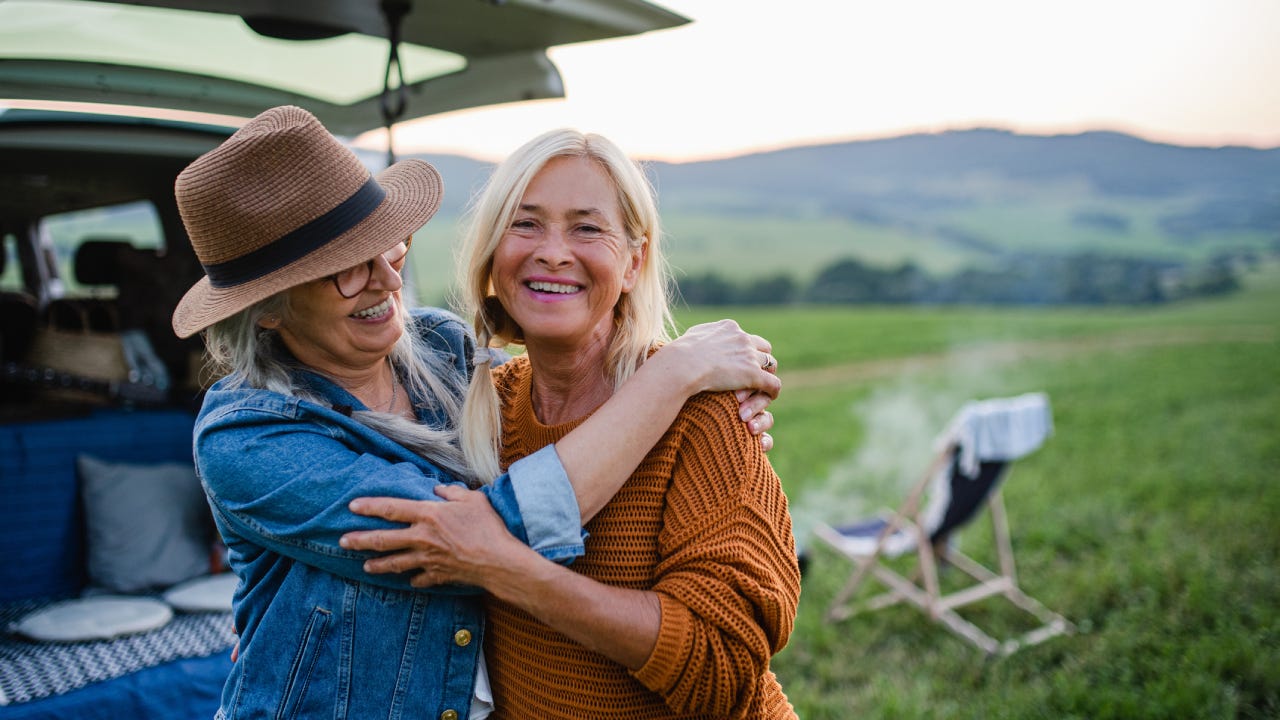 Senior women friends looking at camera outdoors in nature, caravan trip holiday