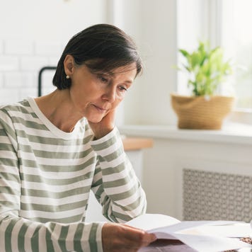 Upset woman thinking about high prices while looking at utilities, gas, electricity, rental charges, water bill due to inflation and crisis. Planning personal budget while sitting in kitchen. Weighing options on how to save money