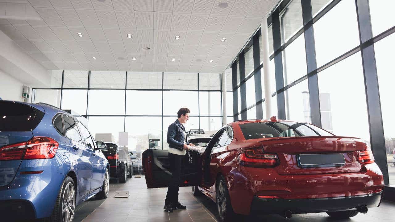 Senior woman looking inside car in showroom