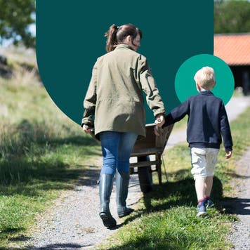 Woman holding a child's hand while steering a wheel barrel