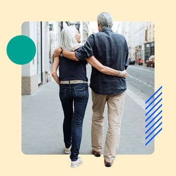 An old couple walking down the sidewalk with their arms around each other's shoulders.