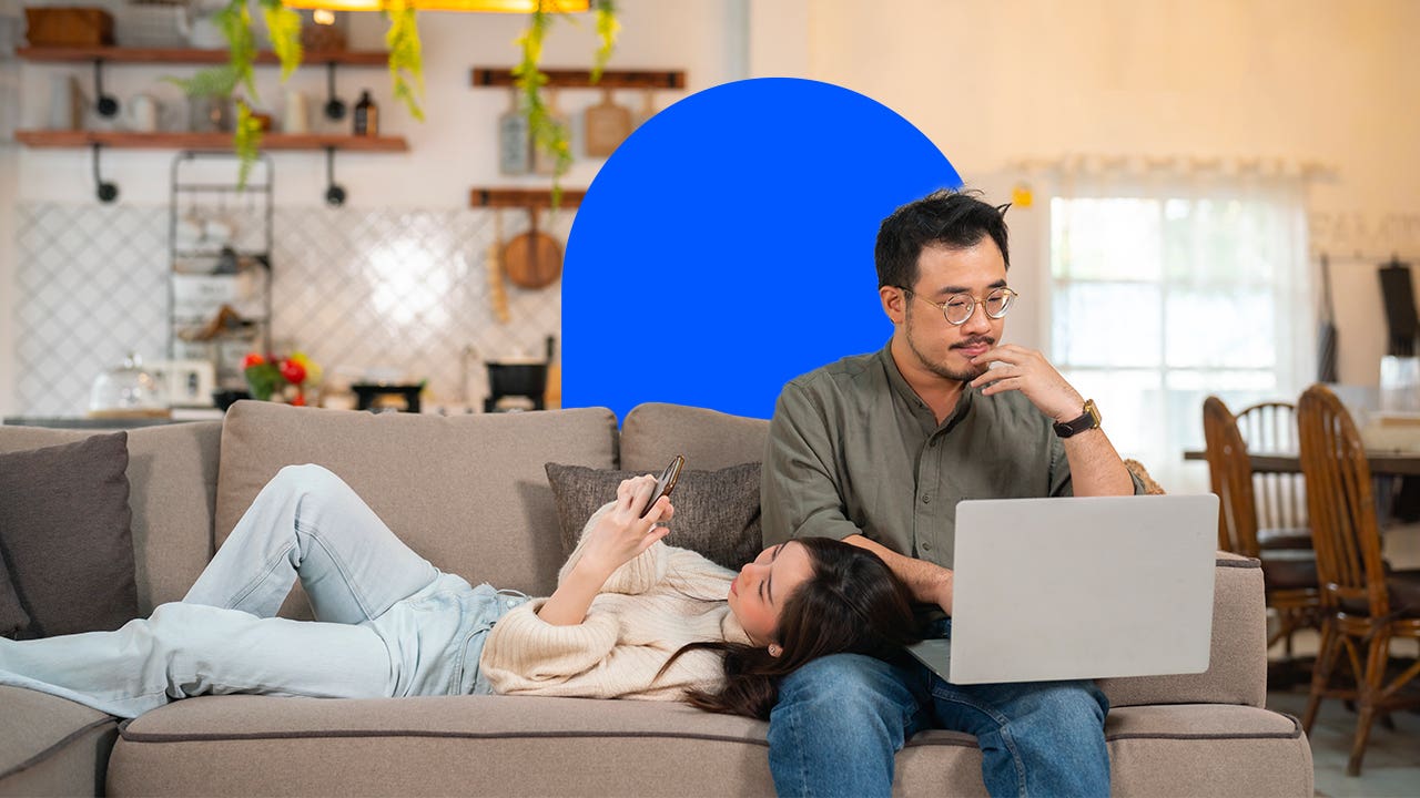 single vs married housing costs - couple sitting on couch looking at phone and laptop