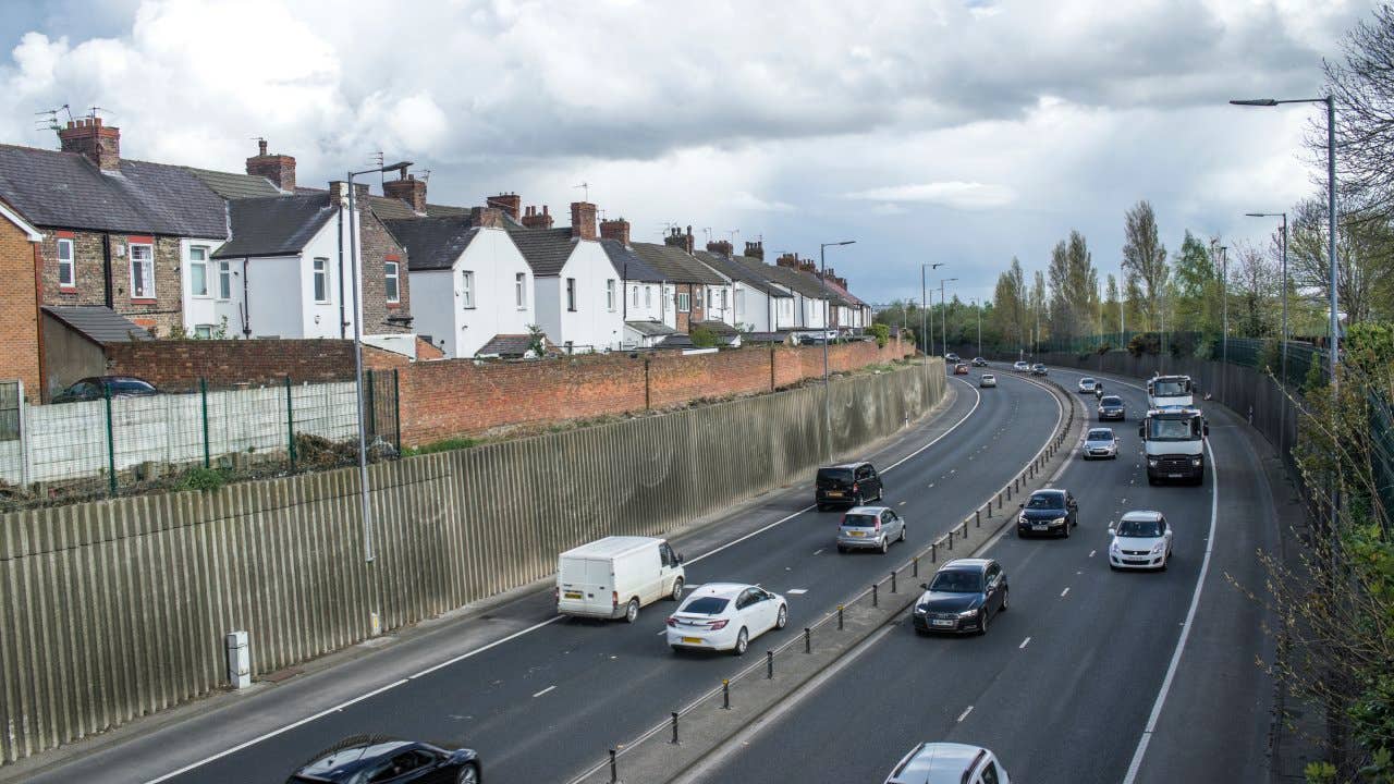 Heavy traffic on dual carriageway continuation of a motorway, passing residential district.