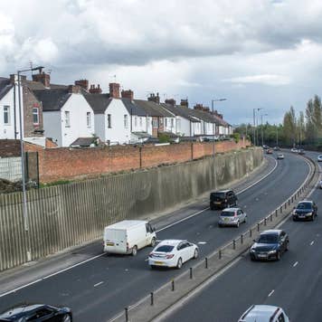 Heavy traffic on dual carriageway continuation of a motorway, passing residential district.