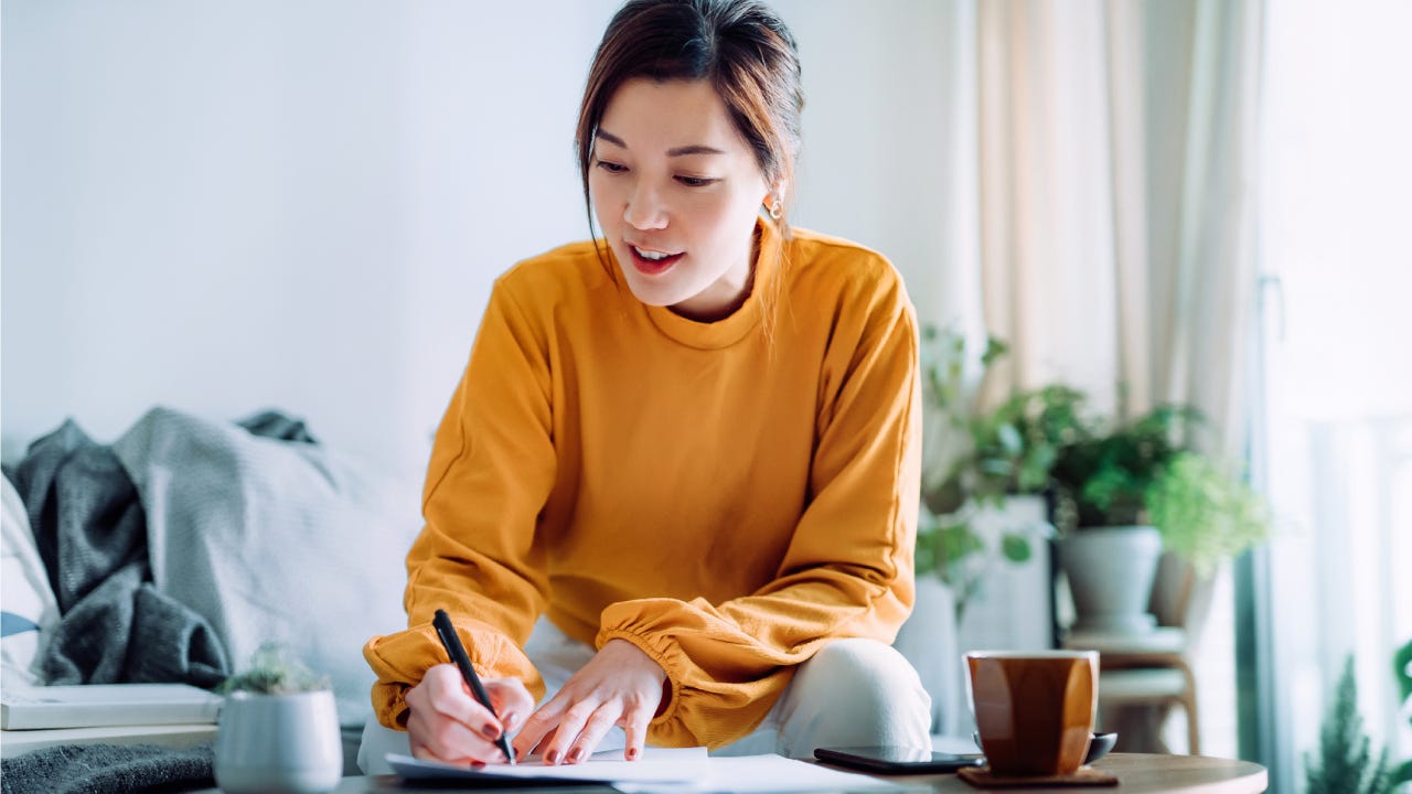 woman holding a pen and signing paperwork in the living room at home