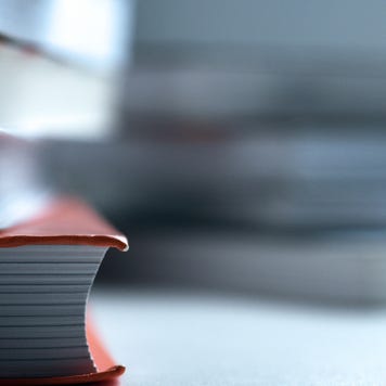 An in-focus stack of books mostly out of frame with a blurry stack of books behind it