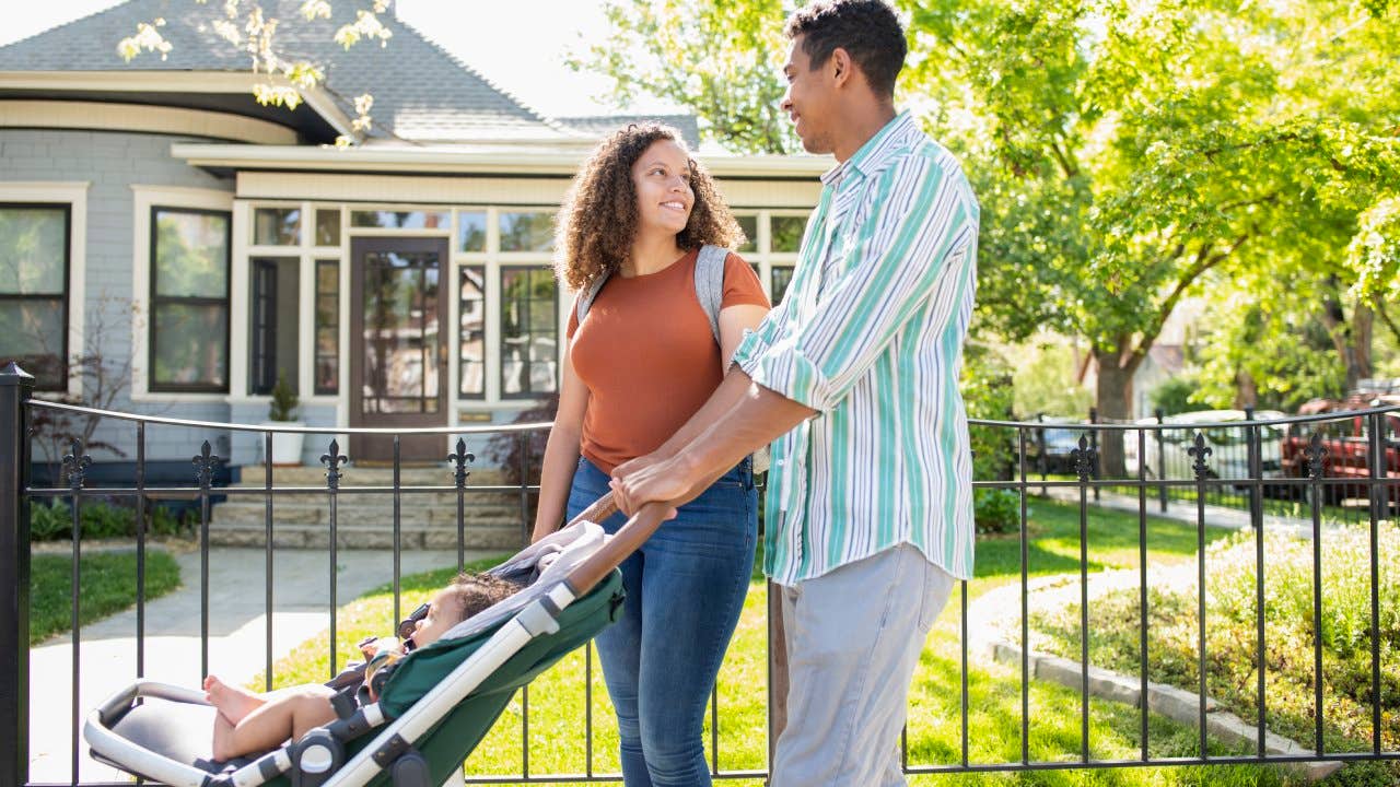 Young mother and father walking with baby daughter in stroller on neighborhood sidewalk